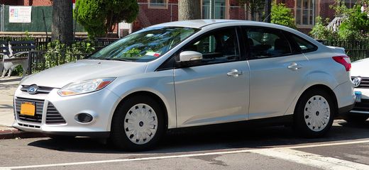 A silver 2014 Ford Focus SE sedan parked on a city street, seen from the front left
