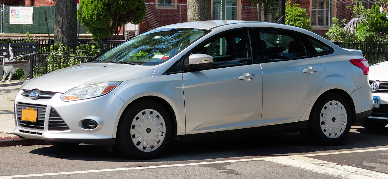 A silver 2014 Ford Focus SE sedan parked on a city street, seen from the front left