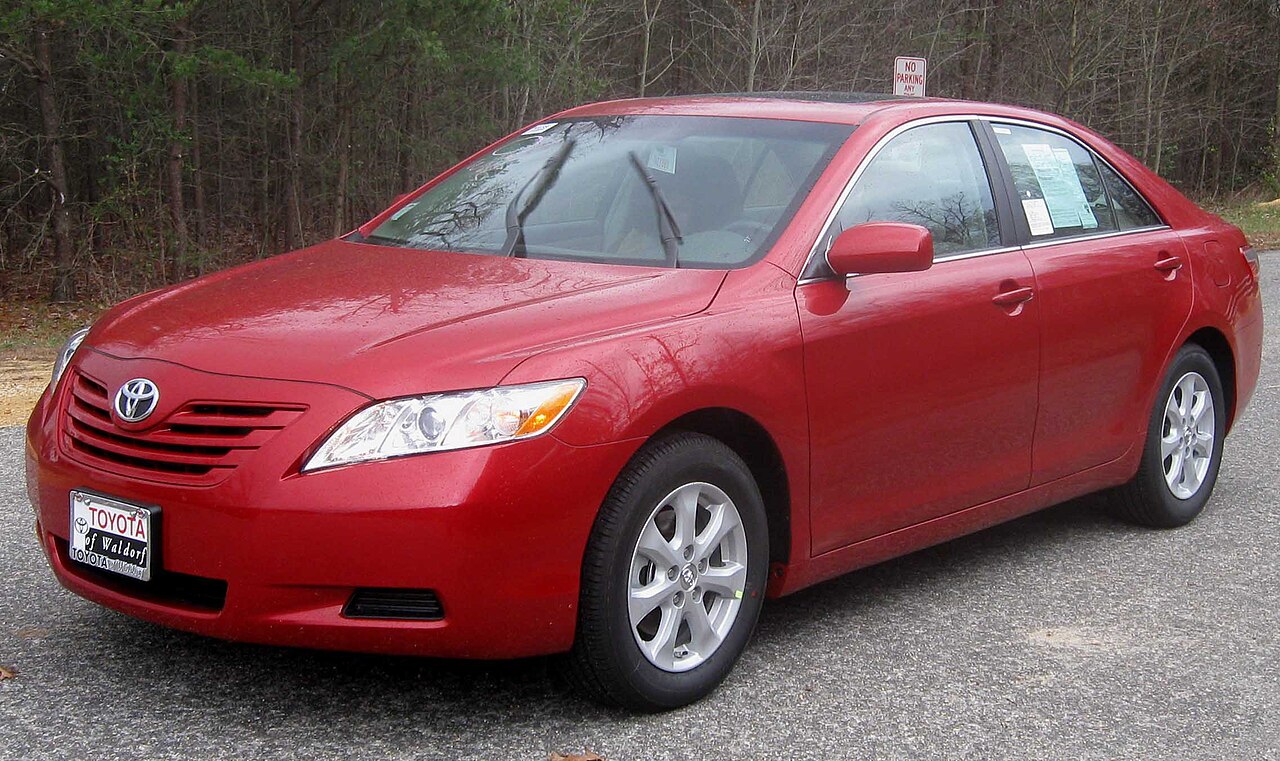 A red 2009 Toyota Camry LE parked on a dealer lot, seen from the front left